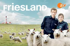 Text: "Friesland" und ein ZDF-Logo. Zwei Polizisten stehen in einer Wiese mit vielen Schafen und einem Leuchtturm im Hintergrund.