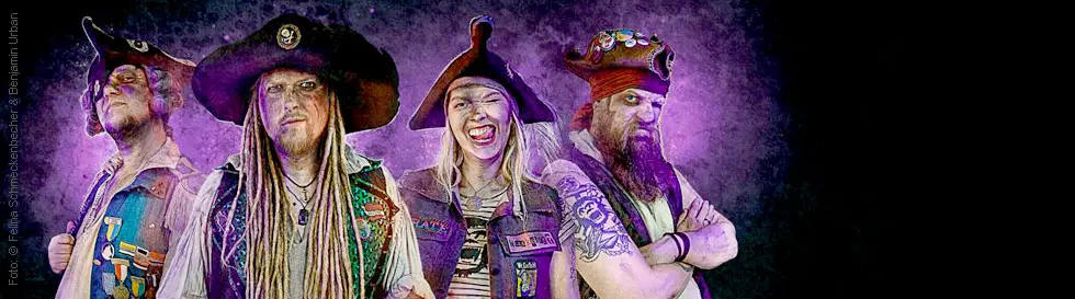 Ein stilisiertes Foto von vier Personen in Piratenkleidung mit lila Hintergrund. Alle tragen Hüte und wirken entschlossen.