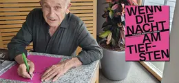 "Wenn die Nacht am tiefsten" steht auf einem pinken Buchcover; links sitzt ein Mann, der das Buchcover signiert.