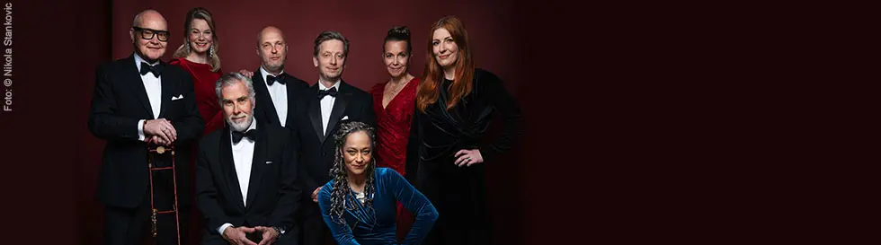 Mehrere Personen in formeller Abendkleidung, vor einem dunklen Hintergrund posierend.