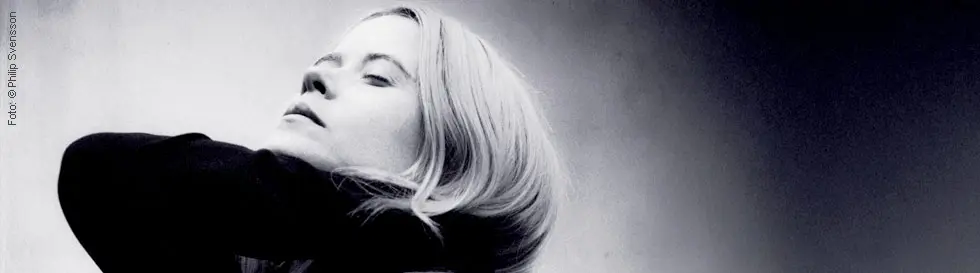 Eine Person mit langen, hellen Haaren blickt mit geschlossenen Augen nach oben.