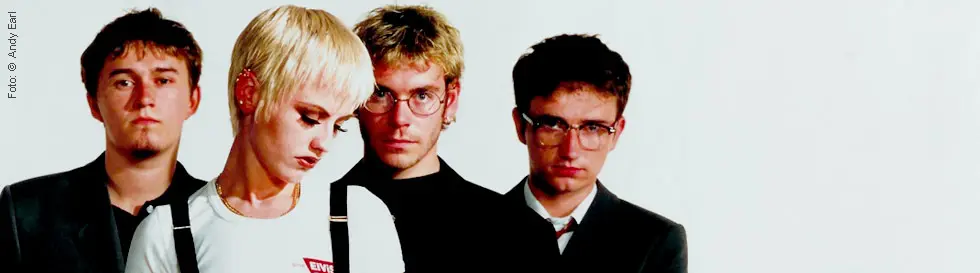 Eine Person mit hellen Haaren trägt ein weißes T-Shirt mit der Aufschrift "LEVI'S". Vier Personen schauen ernst.