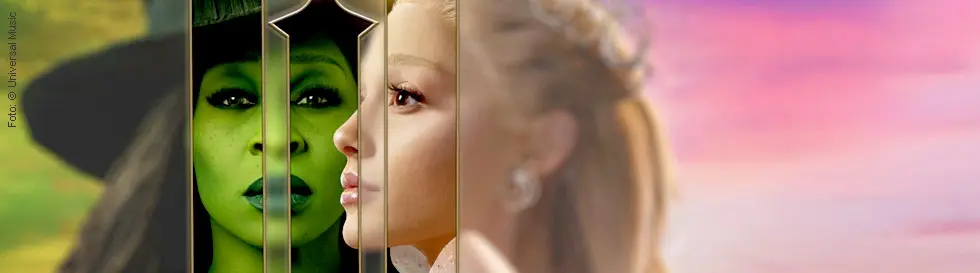 Zwei Gesichter: links grün mit Hut, rechts blass mit Krone, durch goldenen Rahmen getrennt.