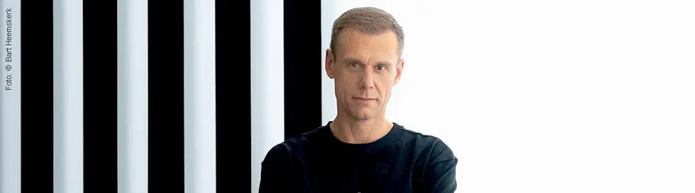 Eine Person in schwarzem Shirt steht vor schwarz-weißen Streifen.