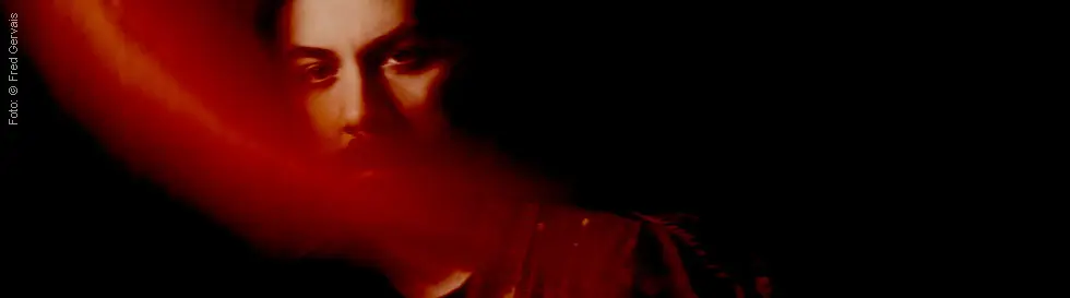 Unklarer, rot getönter Schatten verdeckt das Gesicht einer Person vor schwarzem Hintergrund.