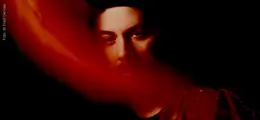 Unklarer, rot getönter Schatten verdeckt das Gesicht einer Person vor schwarzem Hintergrund.