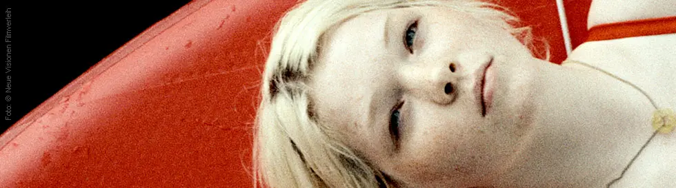 Eine junge Frau mit blonden Haaren liegt auf einem roten Boot. Sie trägt ein rotes Oberteil.