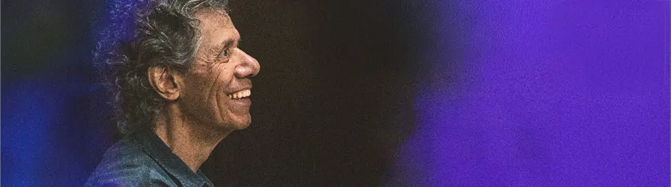 Ein lächelnder Mann im Profil, umgeben von blauen und lila Unschärfen.