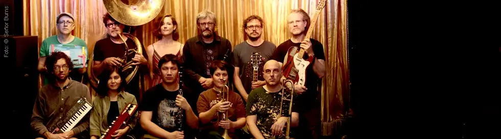 Eine Gruppe von elf Personen mit Musikinstrumenten vor einem goldenen Vorhang.