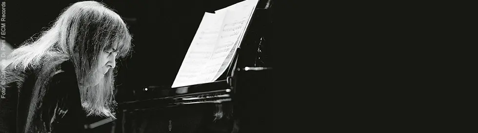 Eine Frau spielt konzentriert Klavier, das Notenblatt ist auf dem Instrument aufgestellt. Schwarz-Weiß-Ästhetik.