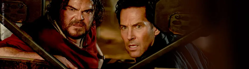 Zwei Männer schauen konzentriert und angespannt durch das hintere Fenster eines Geländewagens.