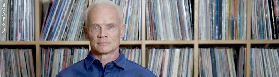 Ein Mann in blauem Hemd steht vor einem Regal mit vielen Schallplatten.