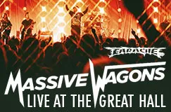"Massive Wagons Live at The Great Hall." Im Hintergrund Konzerteindruck mit orangefarbenen Lichtern und einer Band auf der Bühne.