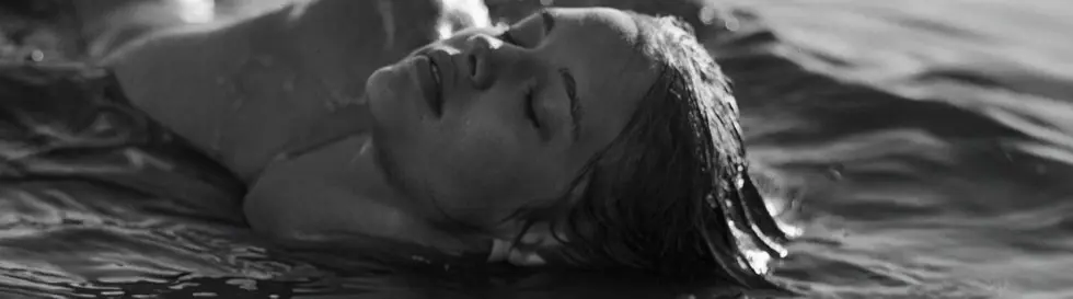 Eine Frau liegt entspannt im Wasser mit geschlossenen Augen. Die Szene ist in Schwarz-Weiß gehalten.