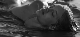 Eine Frau liegt entspannt im Wasser mit geschlossenen Augen. Die Szene ist in Schwarz-Weiß gehalten.