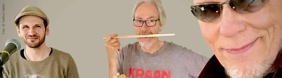 Vier Männer, freundlich lächelnd, zwei mit Instrumenten, einer mit Sonnenbrille.