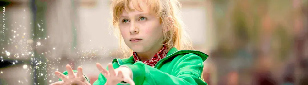 Ein Kind in einer grünen Jacke hält die Hände vor sich, aus denen magisch wirkende Funken strömen.