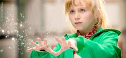 Ein Kind in einer grünen Jacke hält die Hände vor sich, aus denen magisch wirkende Funken strömen.