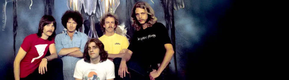 Eine Gruppe von fünf Männern, einige mit T-Shirts mit Motiven und Schriften, posiert vor einem abstrakten Hintergrund.