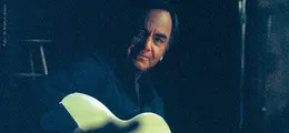 Eine Person mit einer Gitarre in einer dunklen Umgebung.