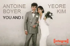 Text: ANTOINE BOYER, YEORE KIM, YOU AND I. Ein Mann im grauen Anzug und eine Frau im weißen Anzug mit einem Blumenstrauß in der Hand lächeln.