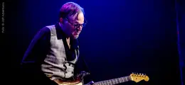 Ein Musiker spielt E-Gitarre in blauem Bühnenlicht.