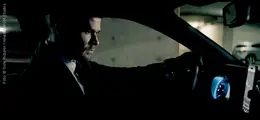 Ein Mann in einem Anzug fährt ein Auto in einer Tiefgarage, das Armaturenbrett leuchtet blau.