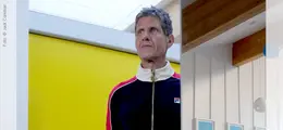 Person in dunkler Trainingsjacke vor gelber Wand, scheinbar in modernem, hellen Raum.