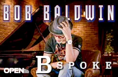 Texte: "Bob Baldwin", "Bespoke". Ein Mann sitzt in einem Sessel, berührt seinen Hut, im Hintergrund ein Flügel.