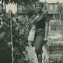 Keine sichtbaren Texte. Eine Frau in einem Garten, trägt ein gestreiftes Kleid und eine Handtasche, lächelt., LP