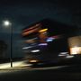 Keine Texte vorhanden. Verschwommener, beleuchteter LKW bei Nacht, vorbei an einer Straßenlaterne und beleuchtetem Gebäude., LP