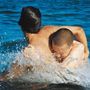 Zwei Personen umarmen sich spielerisch im Wasser, umgeben von spritzenden Wellen.