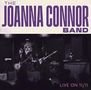Text: "THE JOANNA CONNOR BAND" und "LIVE ON 11/11". Eine Band spielt auf einer Bühne mit Instrumenten., CD