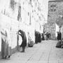 Ein Schwarz-Weiß-Foto zeigt Menschen, die an einer langen, alten Steinmauer beten und sich dabei vorbeugen., CD