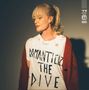 Auf dem zerrissenen T-Shirt steht "ROMANTICIZE THE DIVE". Eine Frau mit blondem Pferdeschwanz trägt es, dazu eine rote Jacke., CD