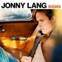 "JONNY LANG SIGNS" steht oben. Ein Mann sitzt nachdenklich in einem Auto, trägt ein Jackett und blickt nach rechts.