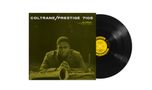 "COLTRANE/PRESTIGE 7105". Ein Mann sitzt ernst mit verschränkten Händen hinter einem Saxophon. Eine Schallplatte daneben.