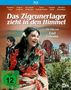 „Das Zigeunerlager zieht in den Himmel“. Ein Film von Emil Loteanu. Eine Frau in bunter Kleidung tanzt, im Hintergrund Planwagen.