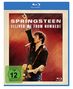 „SPRINGSTEEN: DELIVER ME FROM NOWHERE“. FSK 12-Symbol. Musiker mit Gitarre, singt leidenschaftlich, rote Bühne.