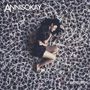 "ANNISOKAY", "ARMS". Frau in Schwarz-Weiß-Kleidung schläft auf einem Bett aus Polaroid-Fotos.