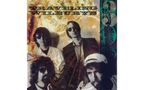 "TRAVELING WILBURYS" in großer Schrift. Vier Männer mit Sonnenbrillen, vor einem abstrakten, erdfarbenen Hintergrund.