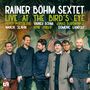 „Rainer Böhm Sextet. Live at the Bird’s Eye. Percy Pursglove, Wanja Slavin, Rainer Böhm, Arne Huber, Jonas Burgwinkel, Domenic Landolf.“ Sechs Männer in dunkler Kleidung stehen vor einer Wand mit tropischem Pflanzenmotiv. Logo unten links., CD
