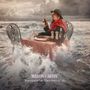 „MARTIN CARTHY – Transform Me Then Into A Fish“. Ein Mann isst an einem Tisch im Meer, Wellen umgeben ihn.