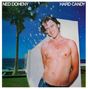 "NED DOHENY" und "HARD CANDY" oben. Ein lächelnder, oberkörperfreier Mann mit Wasserstrahlen, Palme und Meer im Hintergrund.