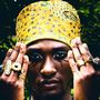Eine Person mit gelbem, gemustertem Turban, dunklem Make-up und mehreren auffälligen Ringen an den Fingern., CD
