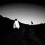 Eine dunkle, bergige Landschaft, vorne eine Person mit Umhang, hinten eine weitere Figur im Gegenlicht., LP