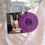 Die Texte: "JOSEFIN ÖHRN CHERRY". Eine Frau in einem glänzenden, gold-rosafarbenen Kleid, mit einer lila Schallplatte., LP