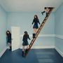 Mehrere Frauen in blauen Kleidern in einem surrealen Raum mit Türen und einer Leiter zur Decke., LP