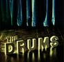 Text: "THE DRUMS". Große 3D-Buchstaben auf einem Holzboden, im Hintergrund ein schwerer, blauer Vorhang., LP