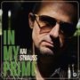 Text: "In My Prime, Kai Strauss." Ein Mann mit Sonnenbrille im Schatten, ernstes Gesicht, leicht gebeugter Kopf.